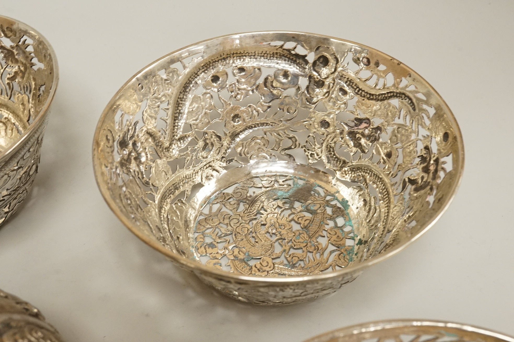 A set of three late 19th/early 20th century Chinese Export pierced white metal bowls, decorated with dragons, by Wang Hing, Hong Kong (lacking glass inserts?), diameter 12.5cm, together with one other similar Chinese Exp